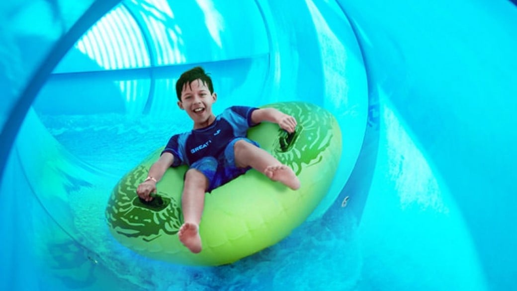 Boy rides down blue waterslide on green tube 