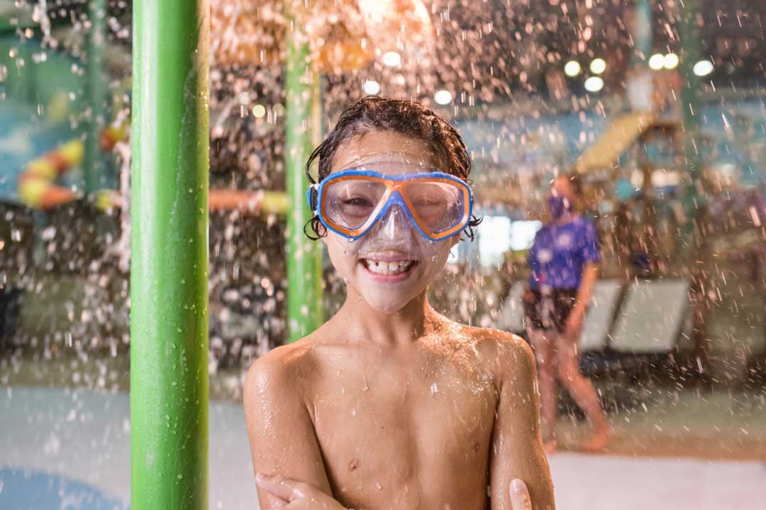 A happy boy standing arms crossed in swim goggles smiling 