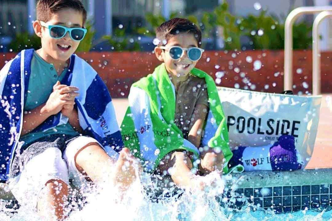 Two kids sitting poolside with sun shades on 