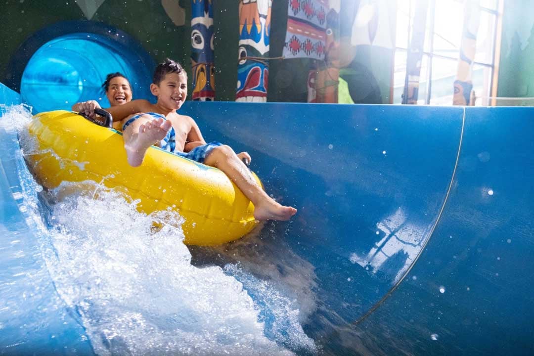 kids sliding down into a pool on a water slide with his mother