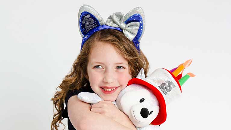 Girl wearing bithday ears and holding a teddy bear