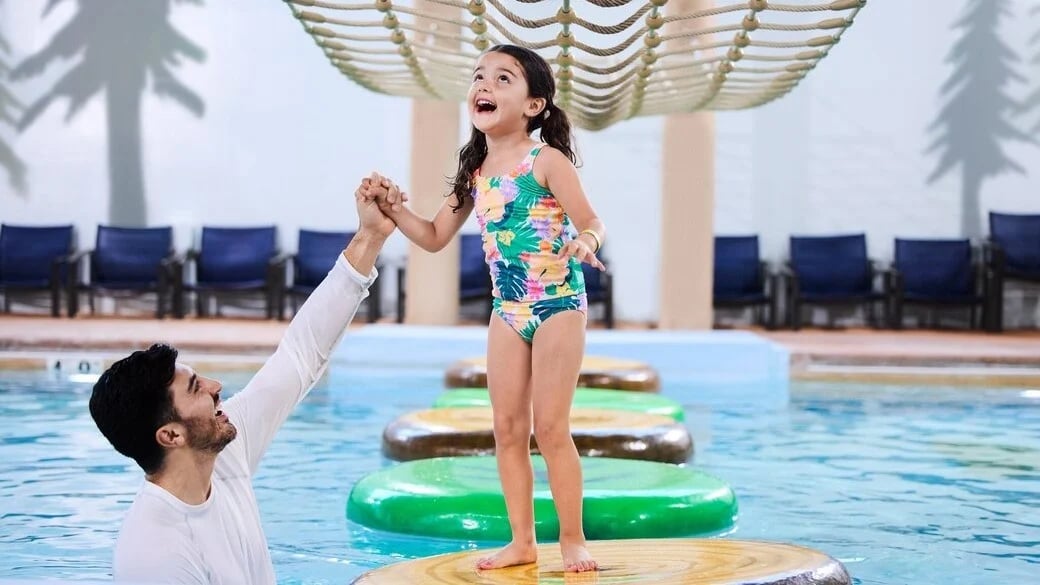 father helping daughter as she crosses the pool