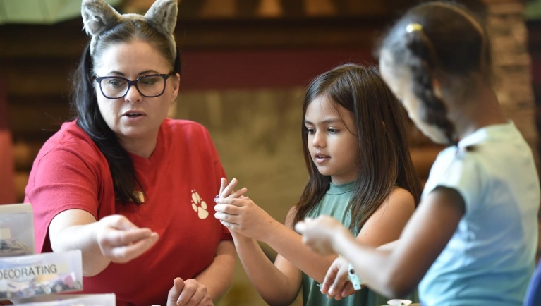 A Great Wolf Lodge pack member helps two girls decorate wolf ears at Camp H.O.W.L.