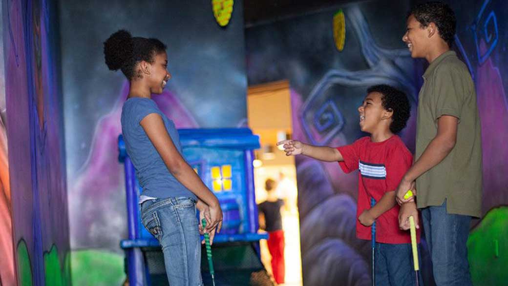 Three kids laughing as they play mini golf