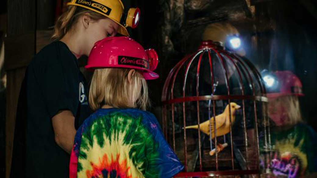 Two girls with mining helmets looking at a bird in a cage