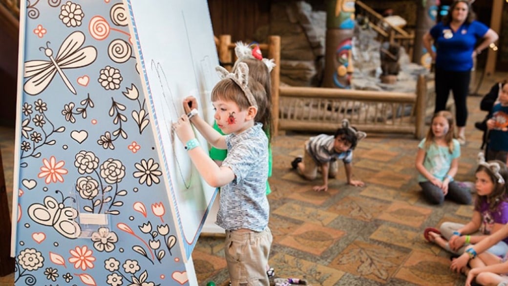 a boy writes on a board as other kids watch