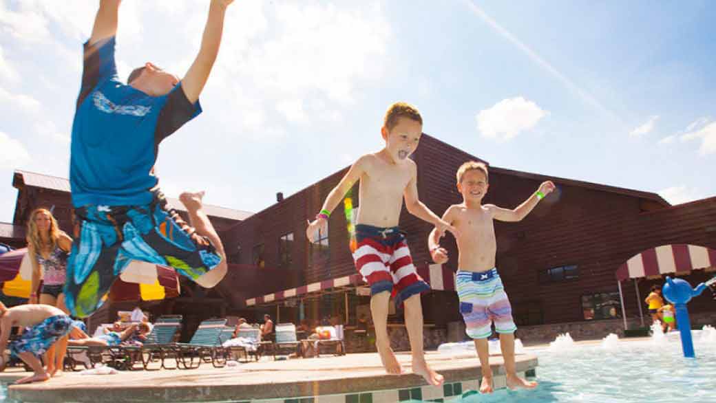 Three boys jump into an outdoor pool at Great Wolf Lodge indoor water park and resort.