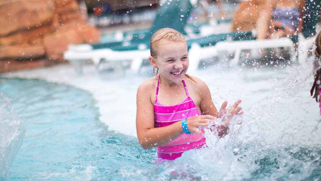 A girl splashes water in an outdoor pool at Great Wolf Lodge indoor water park and resort.