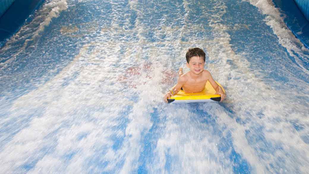 A boy balances on a bodyboard on Wolf Rider Wipeout at Great Wolf Lodge indoor water park and resort.