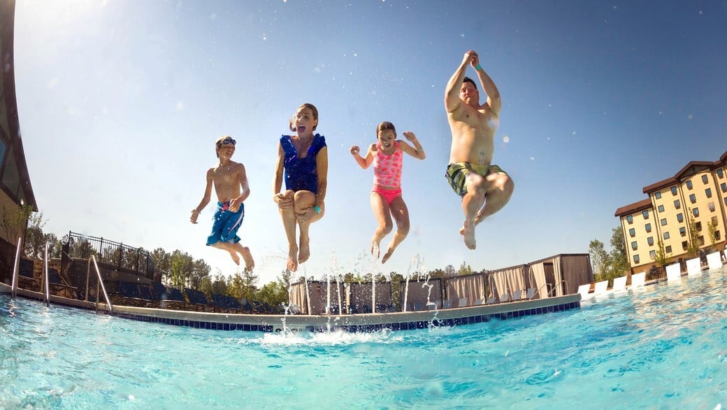 family of four jumping into an outdoor swimming pool