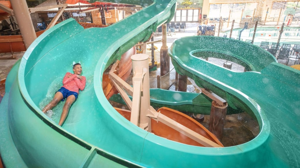 A boy smiles as she rides a water slide